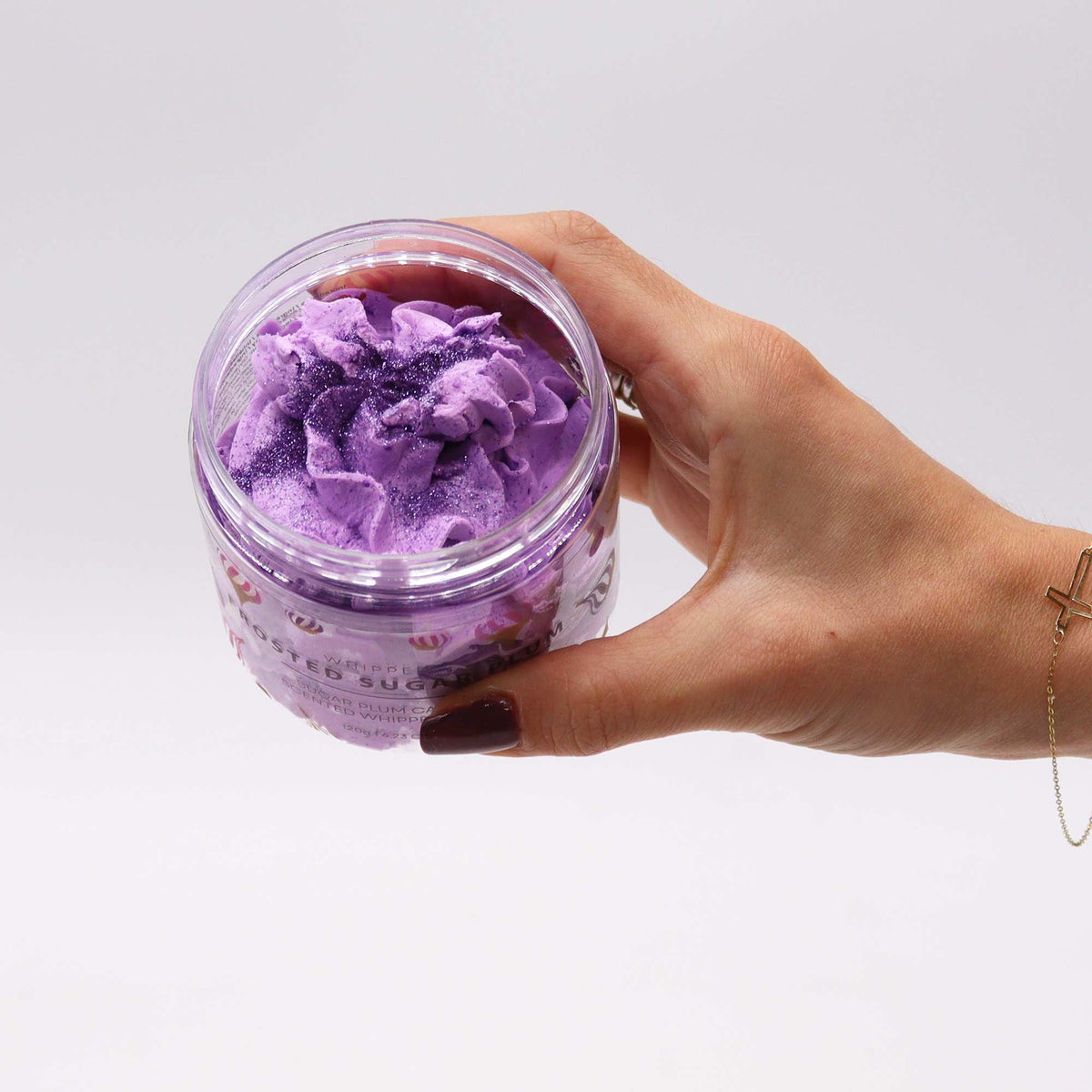 Hand holding a jar of purple whipped soap with a white background