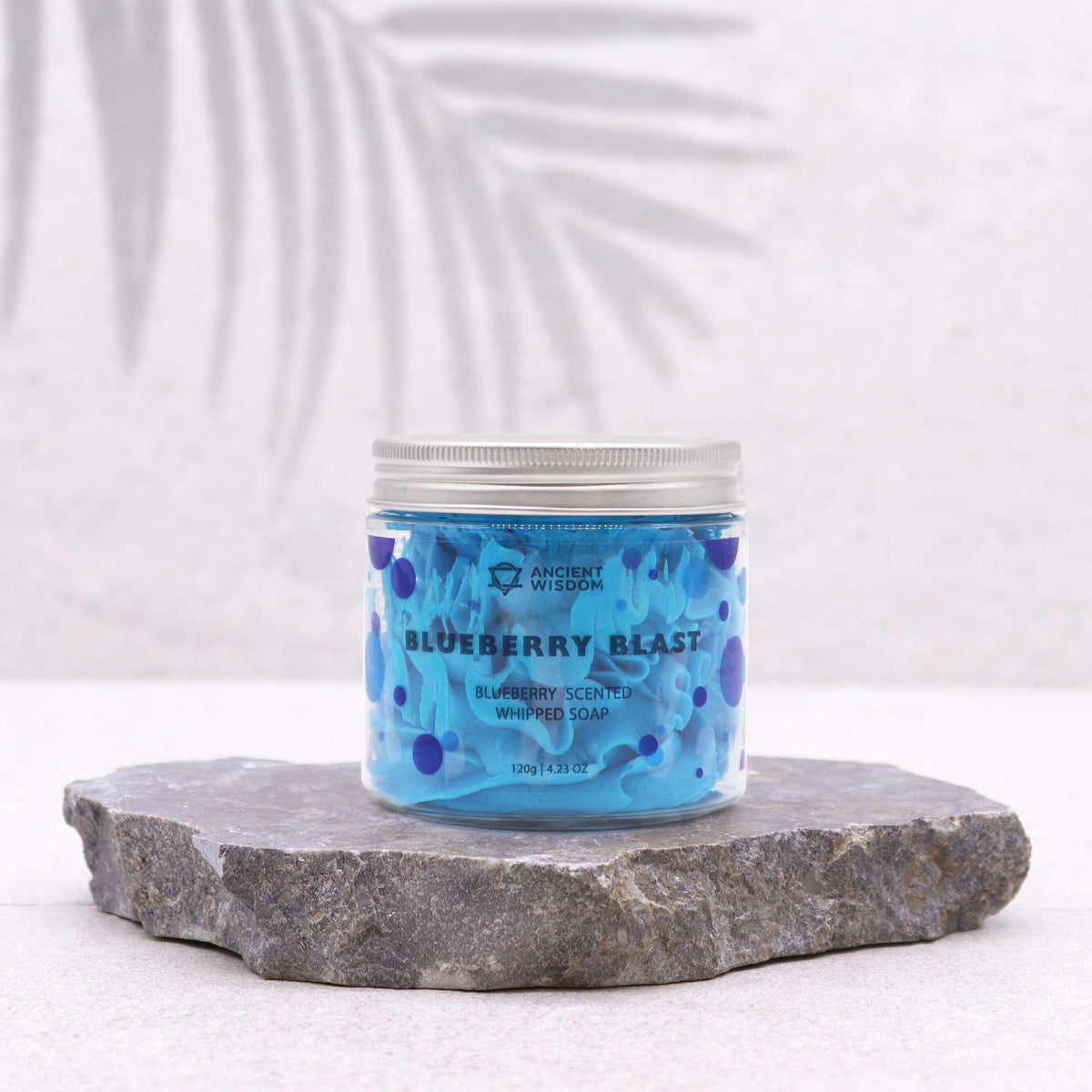 Jar of blueberry-scented whipped soap on a stone surface with a white background
