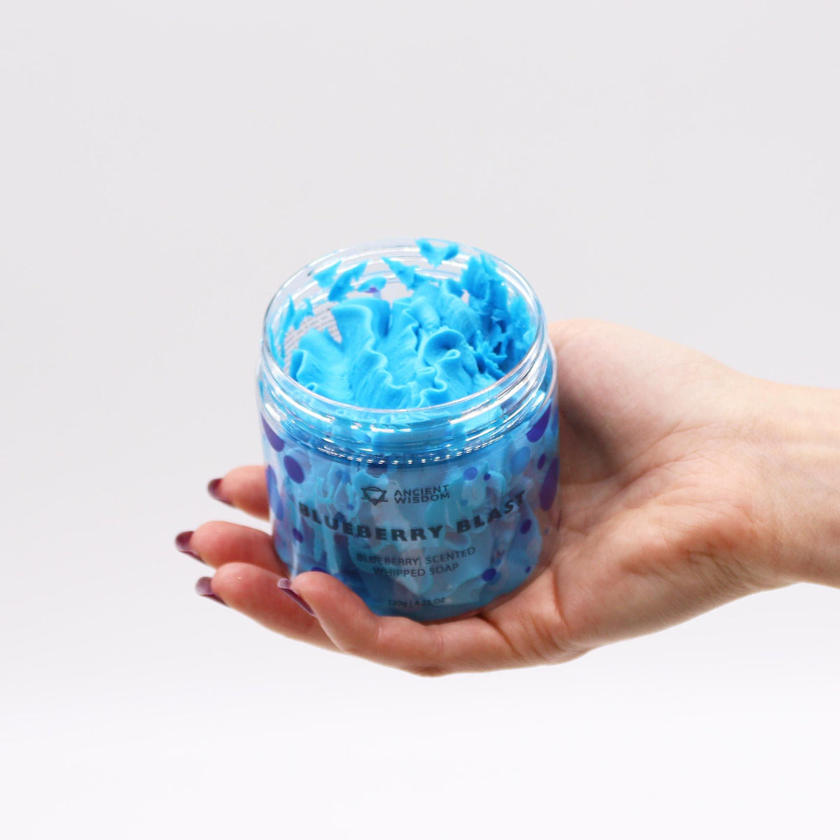 Hand holding a jar of blue bath bomb mixture against a light gray background