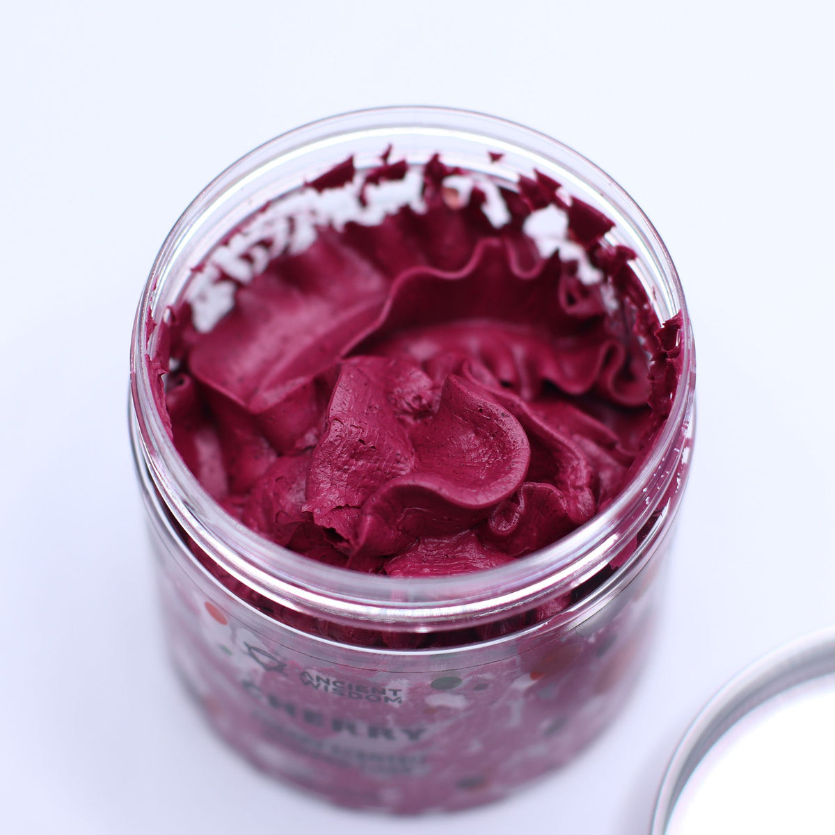 Jar of cherry-coloured whipped soap on a white background