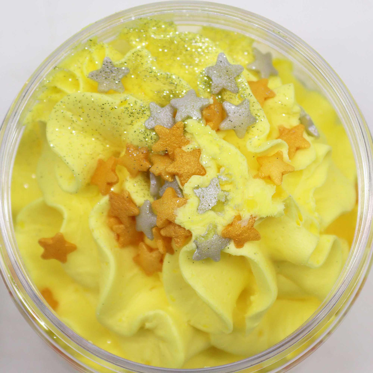 Yellow whipped soap with star-shaped decorations in a clear container on a white background
