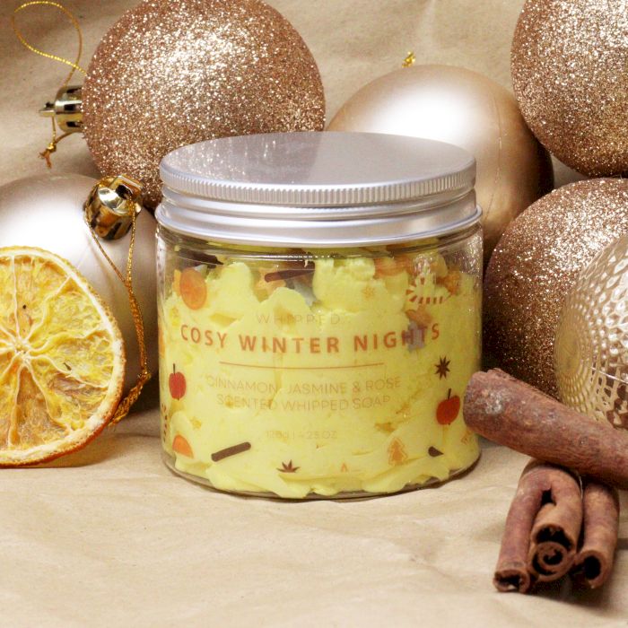 Jar of 'Cosy Winter Nights' candle with Christmas ornaments and cinnamon sticks on a beige background