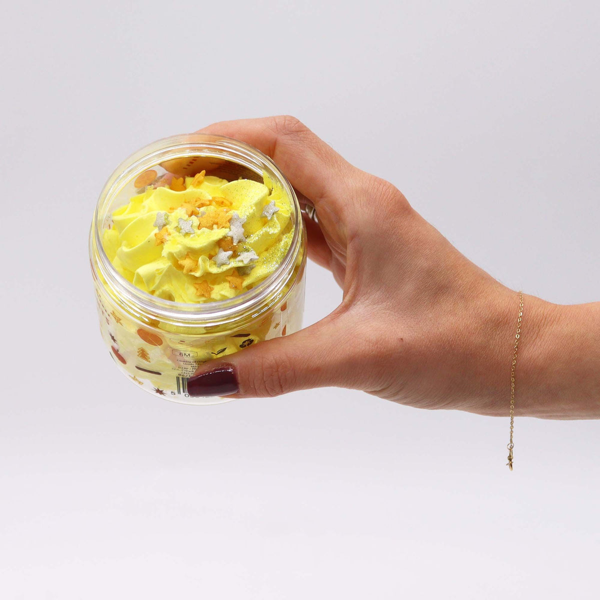 Hand holding a jar of yellow whipped soap with sprinkles on a white background